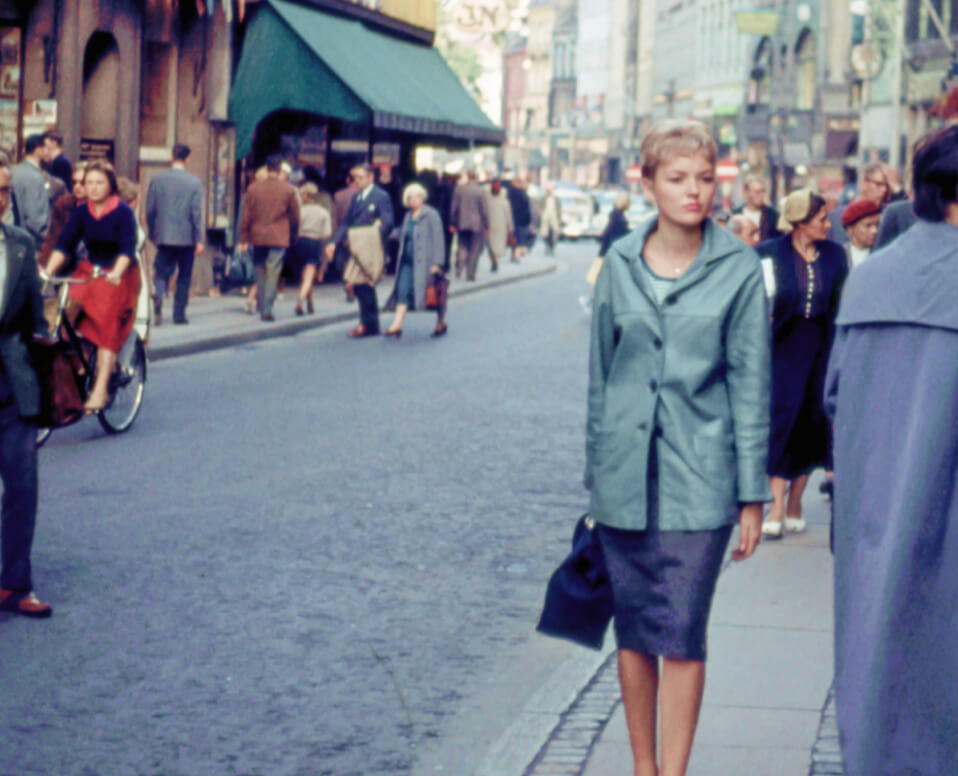 A woman in a blue coat and skirt stands confidently on a bustling city street, embodying urban elegance and style.